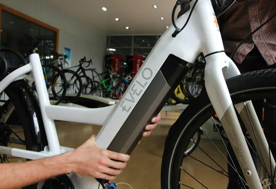 Hand am Akku eines weissen E-Bikes im Laden