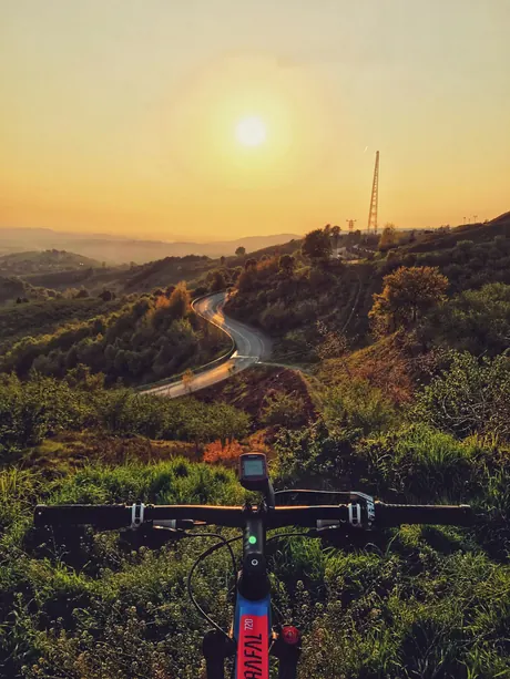 Blick über den Lenker eines Mountainbikes in den Sonnenuntergang, Hochformat